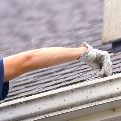 professional with glove on cleaning out gutter